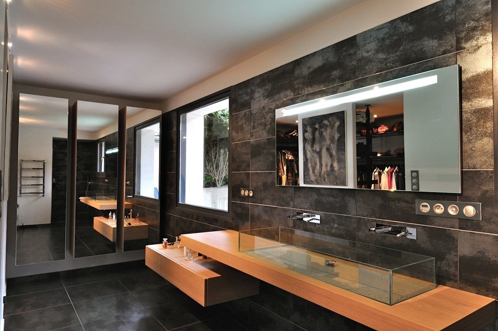 グルノーブルにある高級な広いコンテンポラリースタイルのおしゃれなバスルーム (浴槽なし) (黒いタイル、セラミックタイル、セラミックタイルの床、横長型シンク、木製洗面台、フラットパネル扉のキャビネット、淡色木目調キャビネット、バリアフリー、分離型トイレ、グレーの壁、グレーの床、オープンシャワー、ベージュのカウンター) の写真