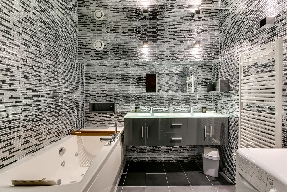 Ejemplo de cuarto de baño principal contemporáneo de tamaño medio con puertas de armario grises, suelo de baldosas de cerámica, lavabo integrado, encimera de vidrio, jacuzzi, baldosas y/o azulejos grises, baldosas y/o azulejos negros y baldosas y/o azulejos con efecto espejo