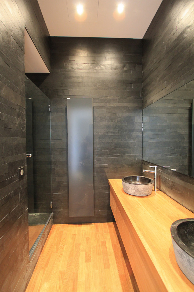 Bild på ett mellanstort funkis badrum med dusch, med en dusch i en alkov, svart kakel, stenkakel, svarta väggar, mellanmörkt trägolv och ett fristående handfat