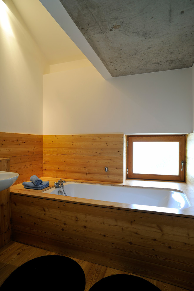 Imagen de cuarto de baño principal industrial de tamaño medio con armarios con paneles lisos, puertas de armario de madera oscura, encimera de madera, bañera empotrada, paredes blancas y suelo de madera en tonos medios