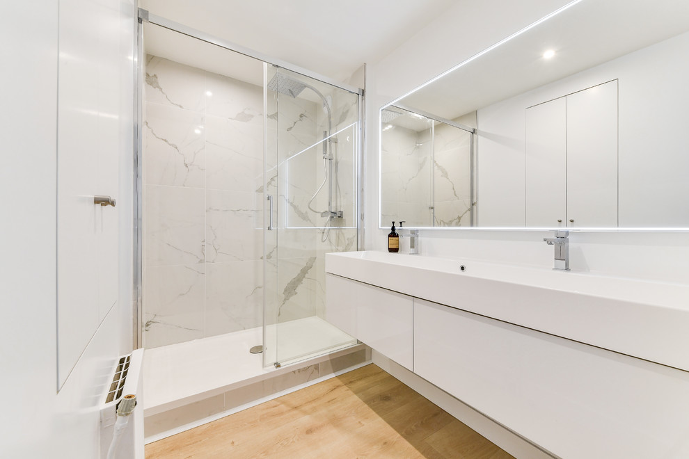 Exempel på ett mellanstort maritimt vit vitt badrum med dusch, med luckor med infälld panel, vita skåp, en öppen dusch, vit kakel, marmorkakel, vita väggar, laminatgolv, ett avlångt handfat, kaklad bänkskiva, brunt golv och med dusch som är öppen