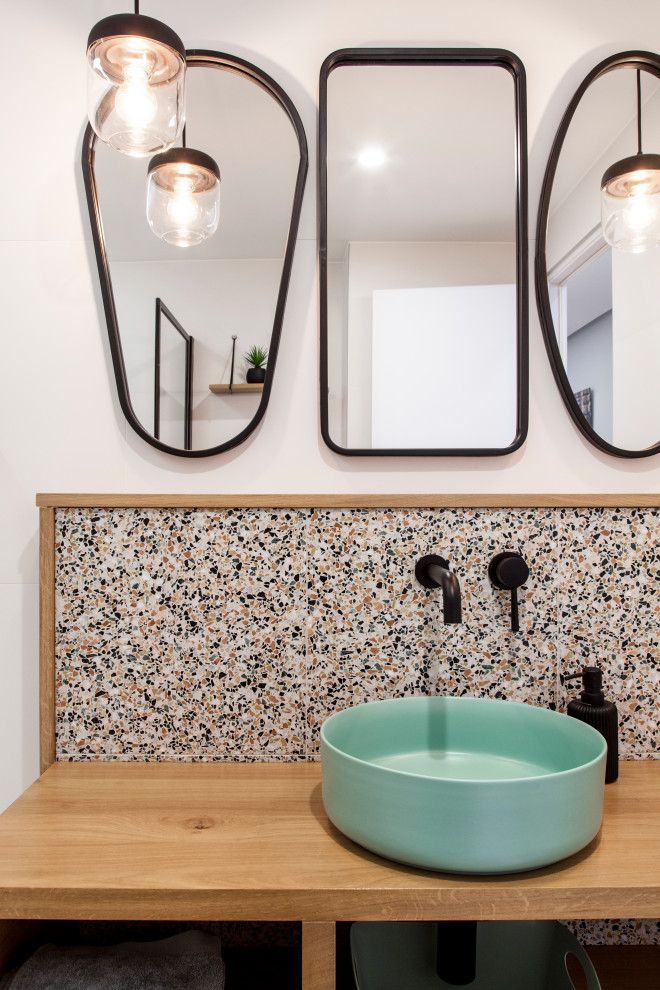 This is an example of a small contemporary ensuite bathroom in Paris with open cabinets, light wood cabinets, a submerged bath, a wall mounted toilet, multi-coloured tiles, ceramic tiles, white walls, ceramic flooring, a vessel sink, wooden worktops and white floors.