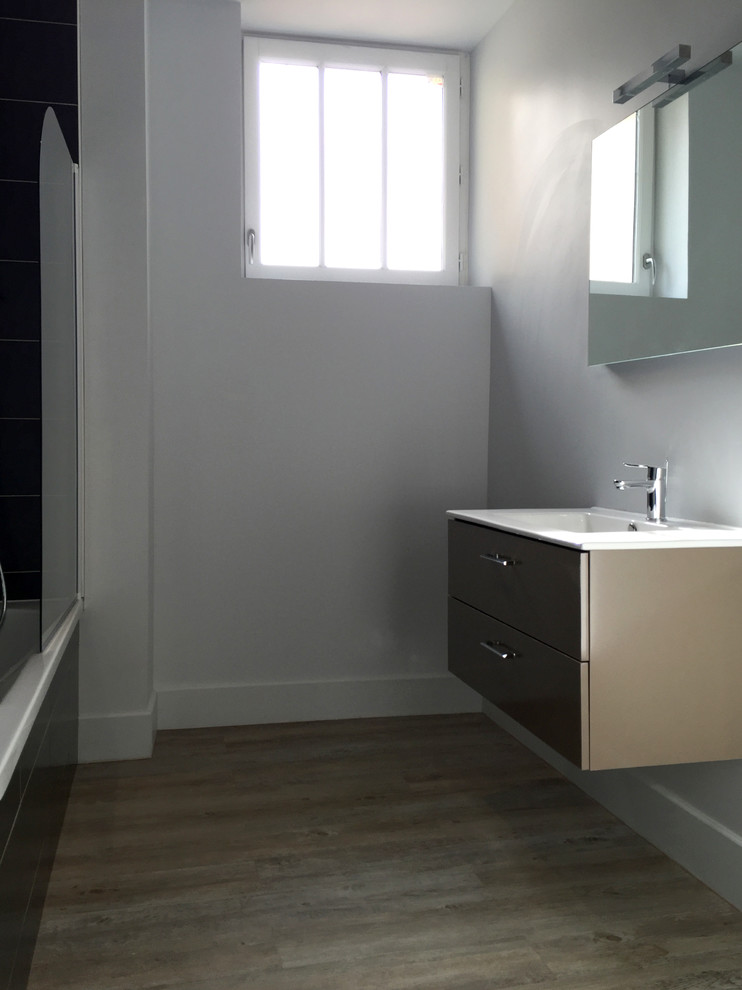 Aménagement d'une salle de bain contemporaine de taille moyenne avec un placard à porte plane, des portes de placard grises, une baignoire encastrée, WC séparés, un mur gris, parquet clair et un lavabo suspendu.