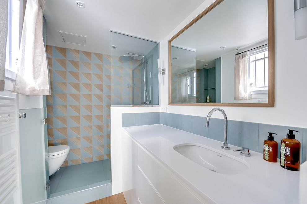 Idée de décoration pour une salle de bain design de taille moyenne avec des portes de placard blanches, WC suspendus, un mur bleu, un sol en bois brun et un lavabo encastré.