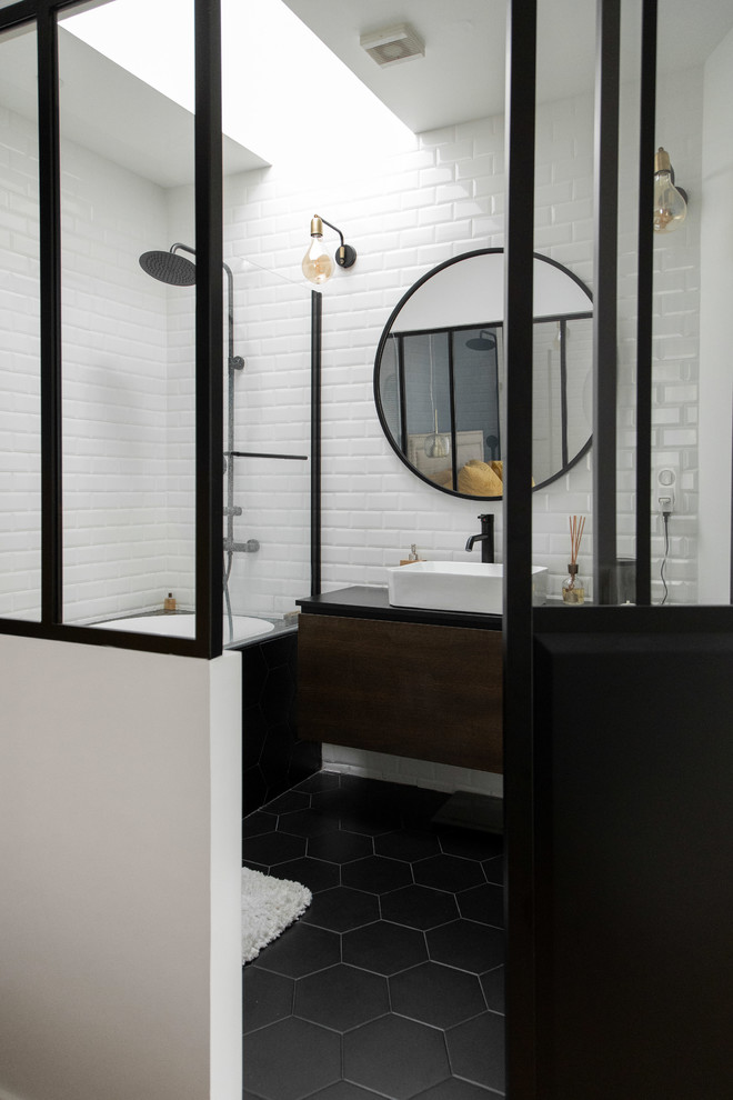 Idéer för att renovera ett mellanstort industriellt svart svart en-suite badrum, med skåp i mörkt trä, ett undermonterat badkar, vit kakel, vita väggar, ett fristående handfat, svart golv, släta luckor, en dusch/badkar-kombination, en toalettstol med separat cisternkåpa, tunnelbanekakel, cementgolv och bänkskiva i akrylsten