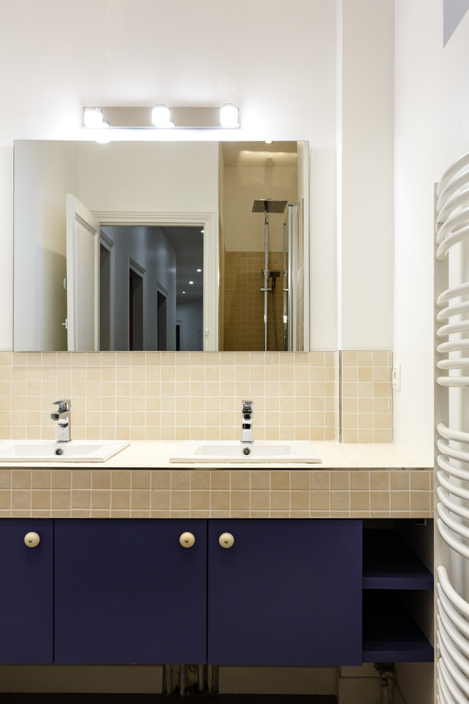 Idéer för mellanstora nordiska gult en-suite badrum, med släta luckor, blå skåp, en dusch i en alkov, en toalettstol med separat cisternkåpa, gul kakel, keramikplattor, vita väggar, ett nedsänkt handfat, kaklad bänkskiva och dusch med gångjärnsdörr