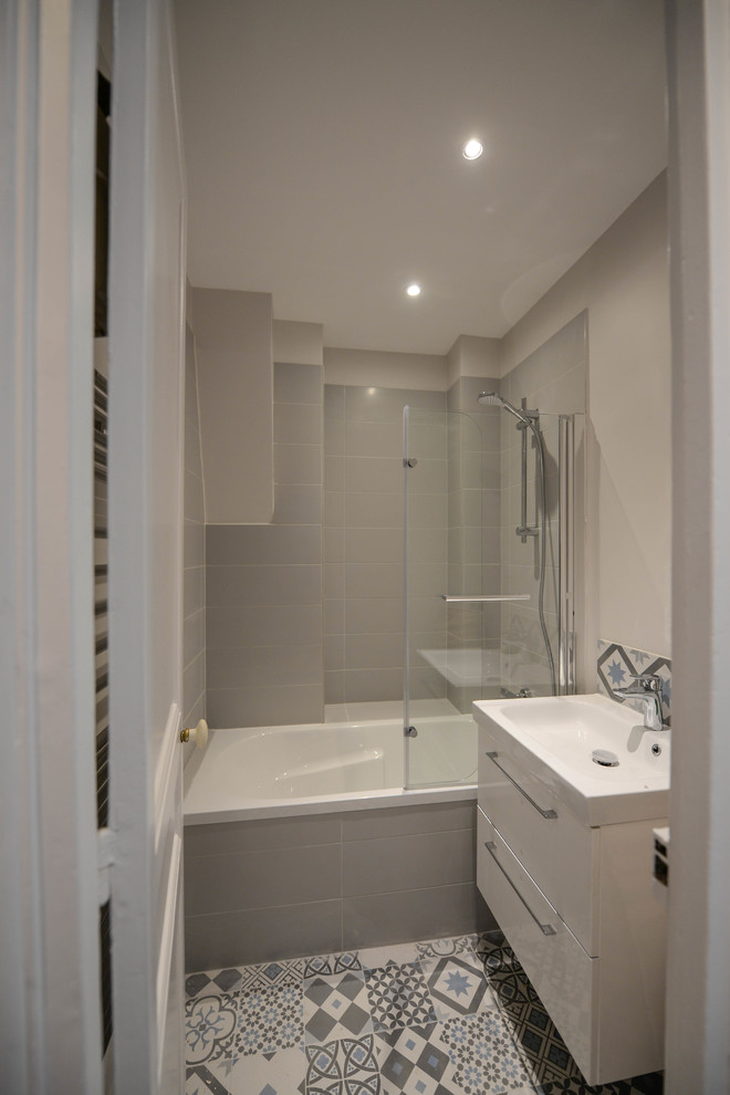 This is an example of a small contemporary ensuite bathroom in Paris with beaded cabinets, white cabinets, a built-in bath, a shower/bath combination, white tiles, grey tiles, ceramic tiles, white walls, cement flooring, a submerged sink, grey floors and an open shower.