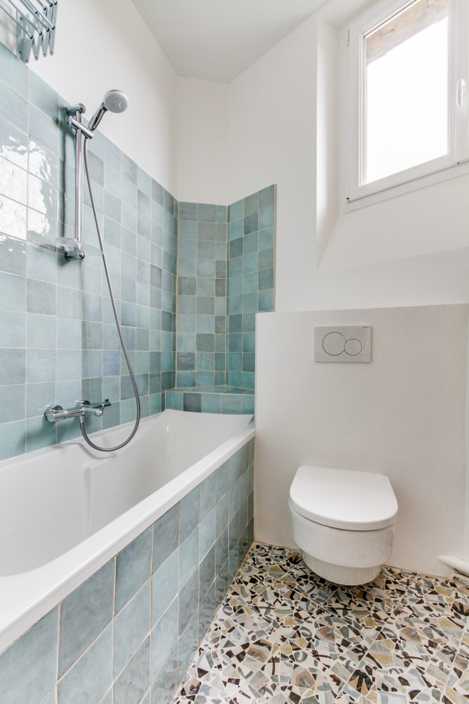 パリにある小さなトランジショナルスタイルのおしゃれな子供用バスルーム (アンダーマウント型浴槽、壁掛け式トイレ、青いタイル、テラコッタタイル、青い壁、セラミックタイルの床、オーバーカウンターシンク、木製洗面台、グレーの床、ベージュのカウンター、ニッチ、洗面台1つ、独立型洗面台) の写真