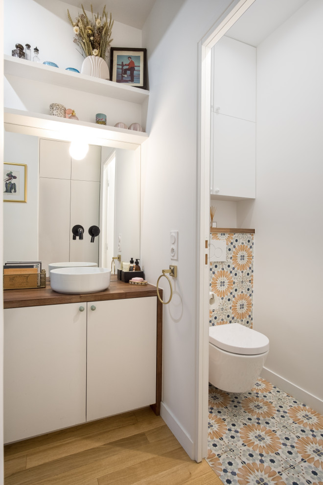Modern inredning av ett brun brunt badrum, med släta luckor, vita skåp, flerfärgad kakel, cementkakel, vita väggar, mellanmörkt trägolv, ett fristående handfat, träbänkskiva och brunt golv