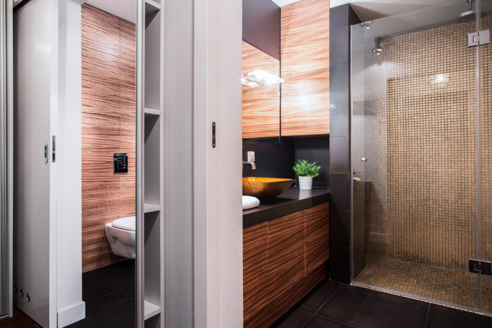 Пример оригинального дизайна: большая ванная комната в современном стиле с плоскими фасадами, фасадами цвета дерева среднего тона, душем в нише, инсталляцией, бежевой плиткой, черными стенами, душевой кабиной, настольной раковиной, черным полом, душем с распашными дверями и черной столешницей