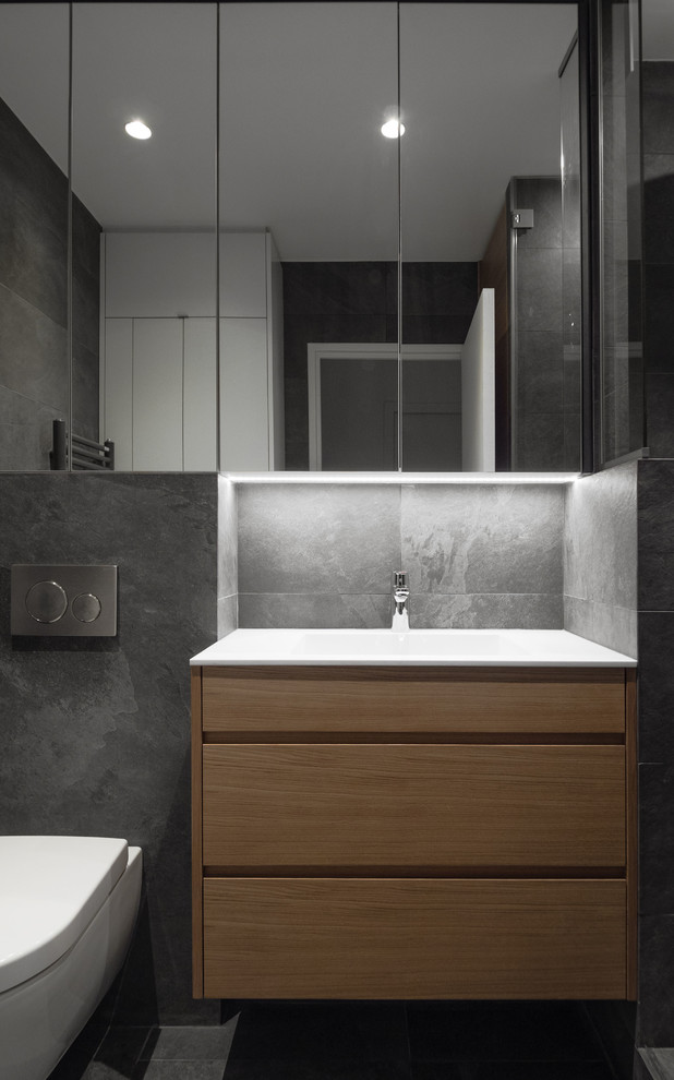 Свежая идея для дизайна: маленькая главная ванная комната в стиле модернизм с фасадами с декоративным кантом, светлыми деревянными фасадами, душем в нише, инсталляцией, серой плиткой, плиткой из сланца, серыми стенами, полом из керамической плитки, врезной раковиной, столешницей из искусственного камня, серым полом, душем с распашными дверями, белой столешницей, тумбой под одну раковину и подвесной тумбой для на участке и в саду - отличное фото интерьера