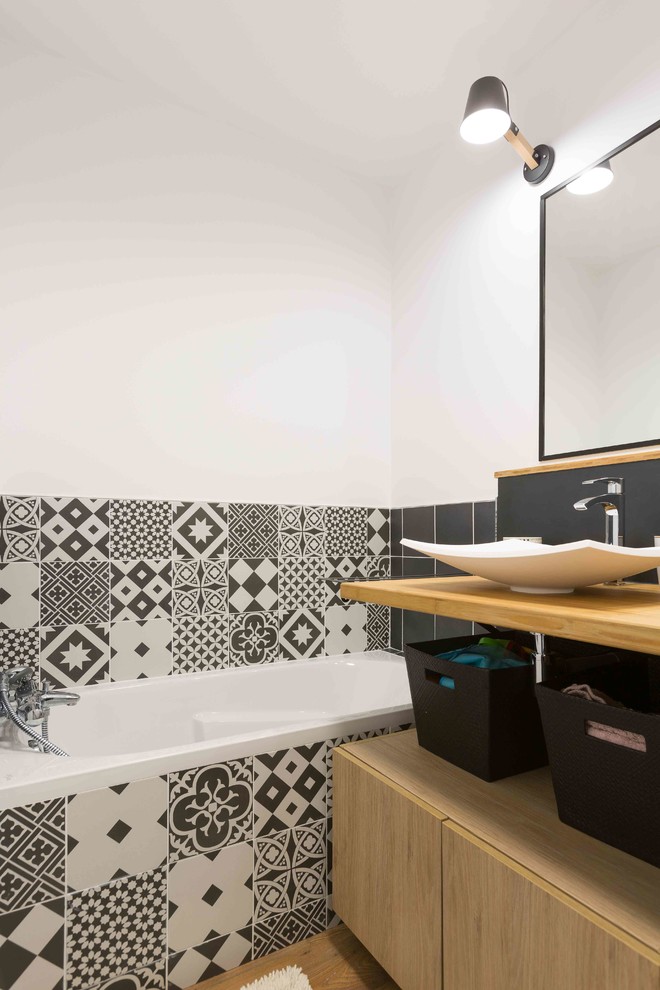 Inspiration pour une petite salle de bain design avec une baignoire encastrée, un carrelage noir et blanc, des carreaux de béton, un mur blanc, un sol en bois brun et une vasque.