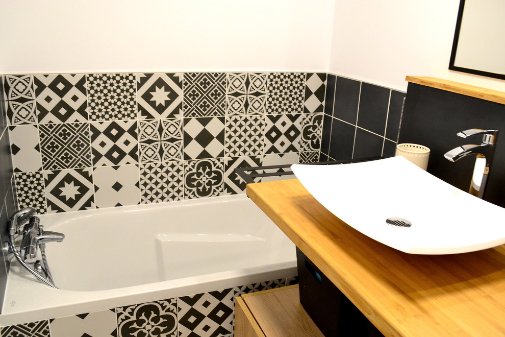Cette photo montre une petite salle de bain tendance pour enfant avec une baignoire encastrée, un carrelage noir et blanc, des carreaux de béton, un mur blanc, un sol en bois brun, un lavabo posé et un plan de toilette en bois.