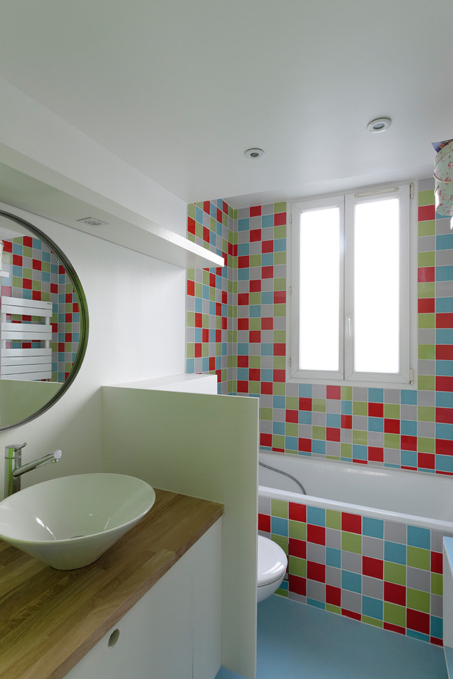 Idéer för att renovera ett mellanstort funkis en-suite badrum, med luckor med profilerade fronter, vita skåp, ett hörnbadkar, en dusch/badkar-kombination, en toalettstol med hel cisternkåpa, vit kakel, blå kakel, röd kakel, grön kakel, porslinskakel, vita väggar, linoleumgolv, ett avlångt handfat, kaklad bänkskiva, blått golv och med dusch som är öppen