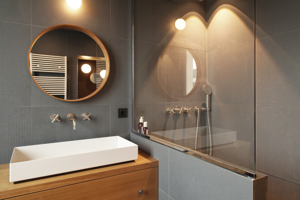 Cette image montre une petite salle de bain design en bois brun avec un carrelage gris, des carreaux de céramique, un mur gris, une grande vasque, un plan de toilette en bois, aucune cabine et un plan de toilette marron.