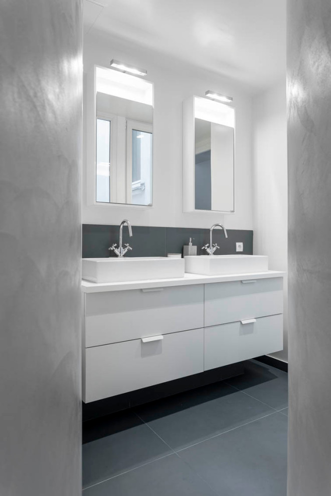 Cette image montre une salle d'eau design de taille moyenne avec un placard à porte plane, des portes de placard blanches, un carrelage gris, des carreaux de porcelaine, un mur blanc, un sol en carrelage de porcelaine, une vasque, un sol gris et un plan de toilette blanc.