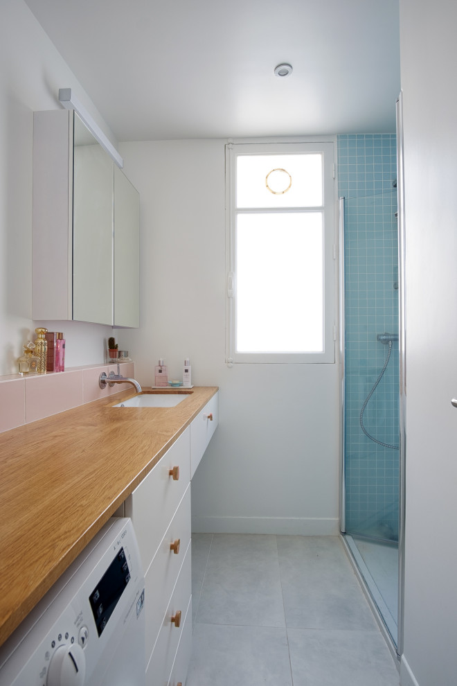 Exempel på ett litet modernt beige beige badrum med dusch, med släta luckor, skåp i mellenmörkt trä, en dusch i en alkov, blå kakel, vita väggar, klinkergolv i porslin, ett undermonterad handfat, träbänkskiva, grått golv och dusch med gångjärnsdörr