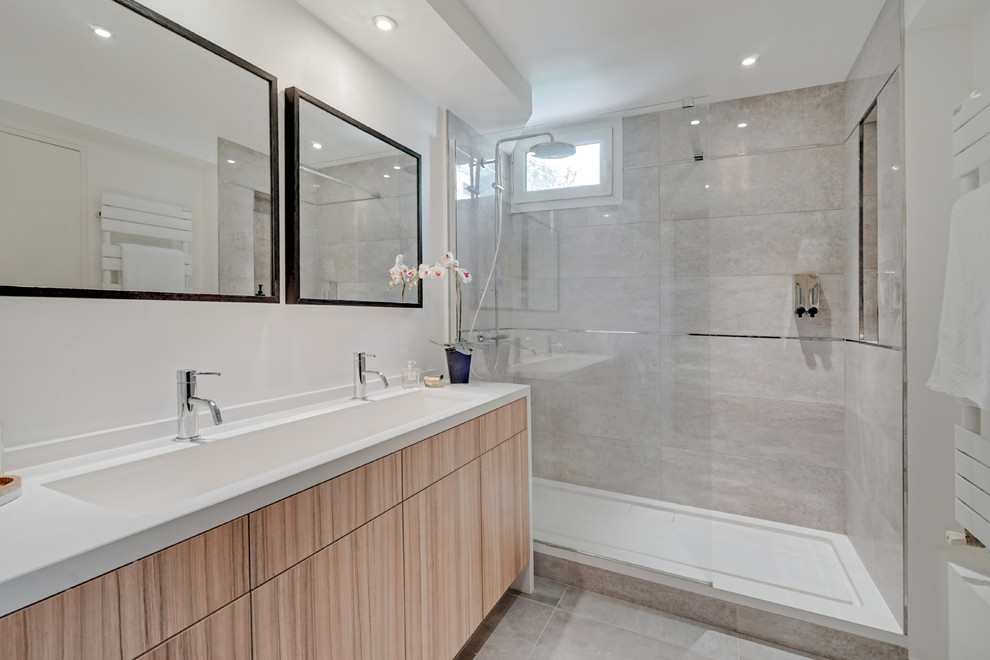 Modernes Badezimmer mit flächenbündigen Schrankfronten, hellbraunen Holzschränken, Duschnische, grauen Fliesen, integriertem Waschbecken, grauem Boden, Schiebetür-Duschabtrennung und weißer Waschtischplatte in Paris