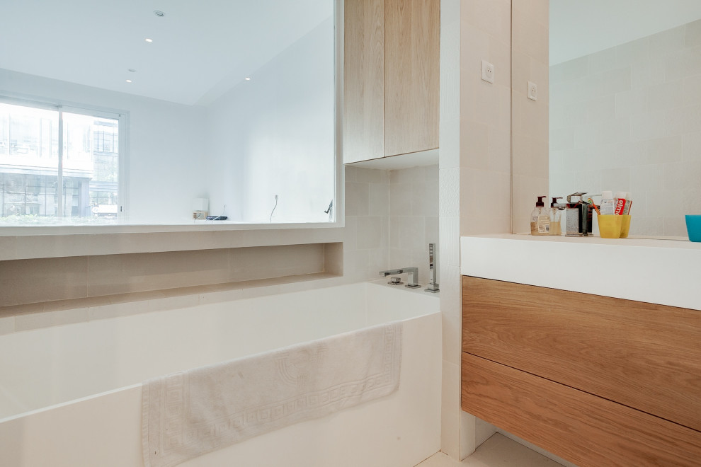 Inredning av ett minimalistiskt mellanstort en-suite badrum, med släta luckor, skåp i ljust trä, ett undermonterat badkar, en vägghängd toalettstol, vit kakel, porslinskakel, vita väggar, cementgolv, ett avlångt handfat, marmorbänkskiva och vitt golv