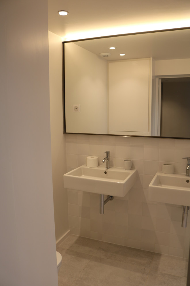 Bild på ett mellanstort funkis badrum, med ett undermonterat badkar, en dusch i en alkov, en vägghängd toalettstol, vit kakel, keramikplattor, vita väggar, klinkergolv i keramik, ett väggmonterat handfat och grått golv