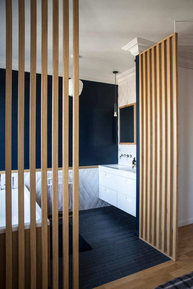 Пример оригинального дизайна: главная ванная комната в современном стиле с плоскими фасадами, белыми фасадами, отдельно стоящей ванной, белой плиткой, черными стенами, монолитной раковиной, черным полом и белой столешницей