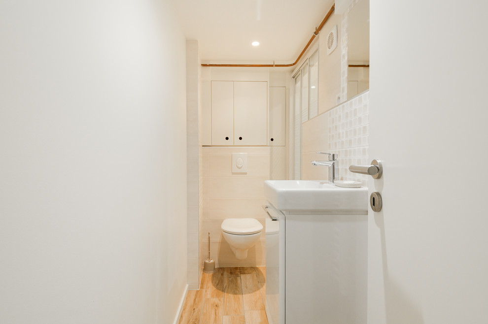 Inredning av ett modernt litet badrum med dusch, med vita skåp, en vägghängd toalettstol, ett väggmonterat handfat, en dusch i en alkov, beige kakel, vita väggar, klinkergolv i keramik och dusch med skjutdörr