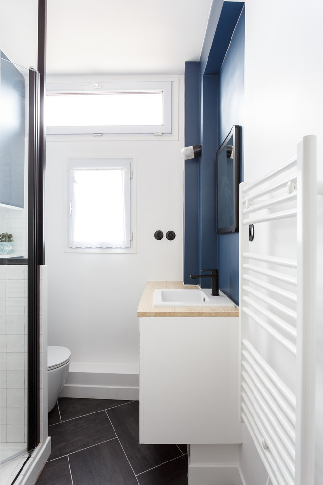 Réalisation d'une petite salle de bain principale minimaliste avec un placard à porte plane, des portes de placard bleues, une douche à l'italienne, WC suspendus, un carrelage blanc, des carreaux de céramique, un mur bleu, un sol en carrelage de céramique, un lavabo posé, un plan de toilette en bois, un sol gris, une cabine de douche à porte battante et un plan de toilette beige.