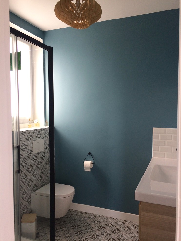 Photo of a small contemporary shower room bathroom in Paris with shaker cabinets, light wood cabinets, a corner shower, a wall mounted toilet, white tiles, metro tiles, blue walls, cement flooring, a submerged sink, tiled worktops, grey floors, a sliding door and white worktops.