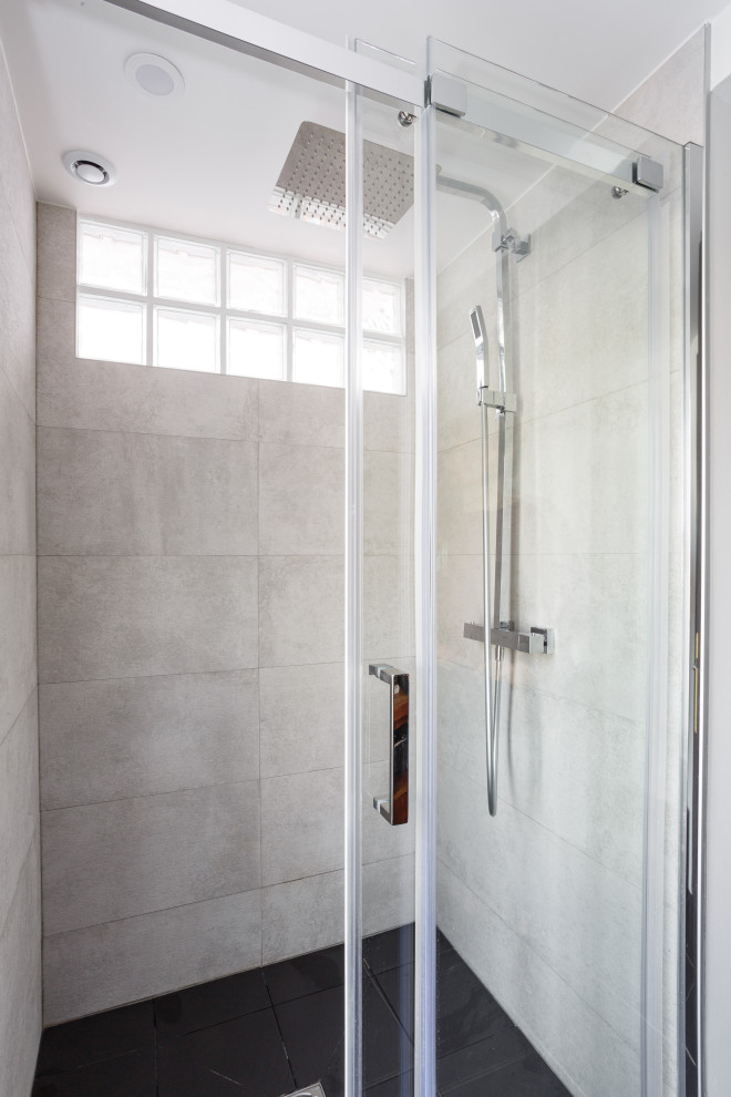 Modern inredning av ett litet brun brunt badrum med dusch, med vita skåp, en kantlös dusch, grå kakel, keramikplattor, vita väggar, klinkergolv i keramik, ett konsol handfat, träbänkskiva, svart golv och dusch med skjutdörr