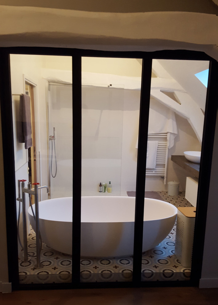 Lantlig inredning av ett stort badrum med dusch, med ett platsbyggt badkar, en kantlös dusch, vita väggar, cementgolv, ett avlångt handfat och med dusch som är öppen
