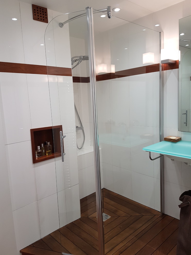 Idéer för små funkis blått badrum med dusch, med luckor med profilerade fronter, vita skåp, en öppen dusch, vit kakel, keramikplattor, vita väggar, mörkt trägolv, ett avlångt handfat, bänkskiva i glas, brunt golv och dusch med gångjärnsdörr