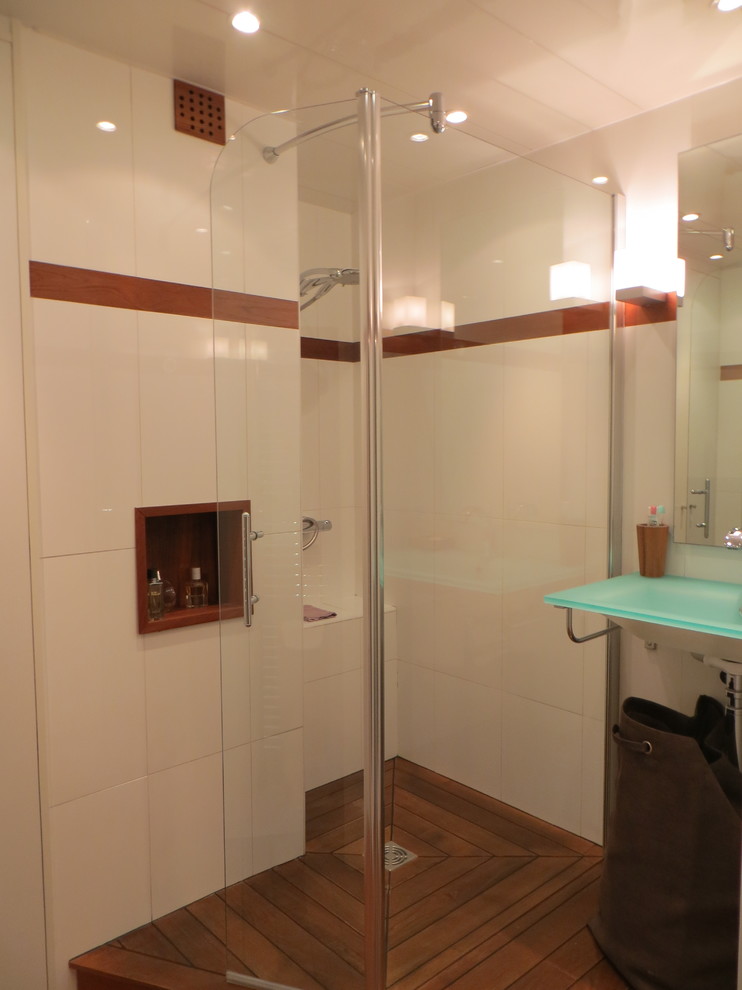 Inredning av ett modernt litet blå blått badrum med dusch, med luckor med profilerade fronter, vita skåp, en öppen dusch, vit kakel, keramikplattor, vita väggar, mörkt trägolv, ett avlångt handfat, bänkskiva i glas, brunt golv och dusch med gångjärnsdörr