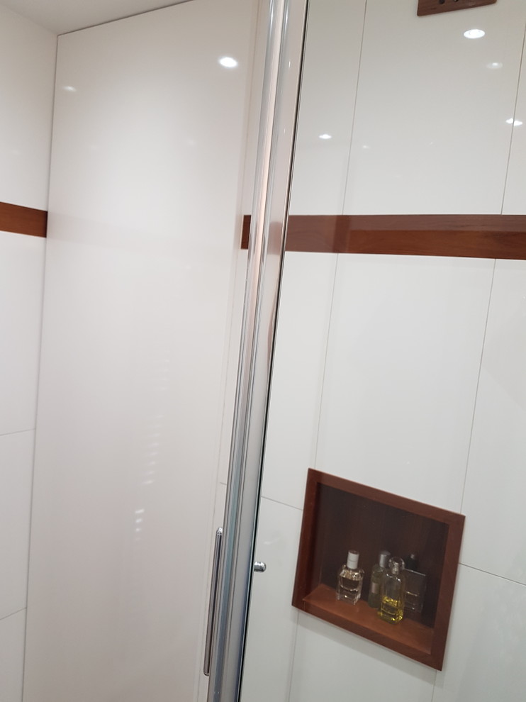Пример оригинального дизайна: маленькая ванная комната в современном стиле с фасадами с декоративным кантом, белыми фасадами, открытым душем, белой плиткой, керамической плиткой, белыми стенами, темным паркетным полом, душевой кабиной, раковиной с несколькими смесителями, стеклянной столешницей, коричневым полом, душем с распашными дверями и синей столешницей для на участке и в саду