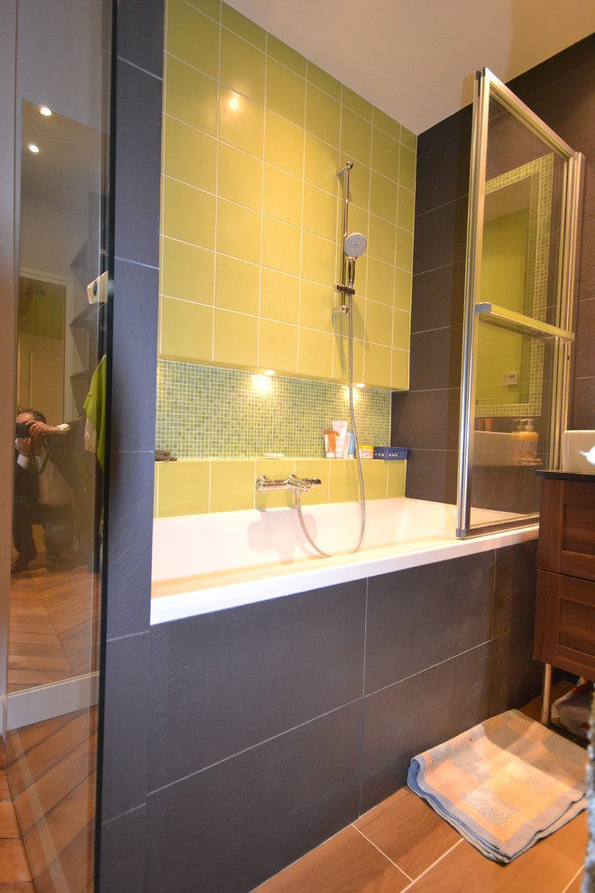 Cette photo montre une salle de bain principale tendance avec une baignoire posée, un combiné douche/baignoire, un carrelage vert, des carreaux de céramique, un mur vert, un sol en bois brun, un lavabo posé et aucune cabine.