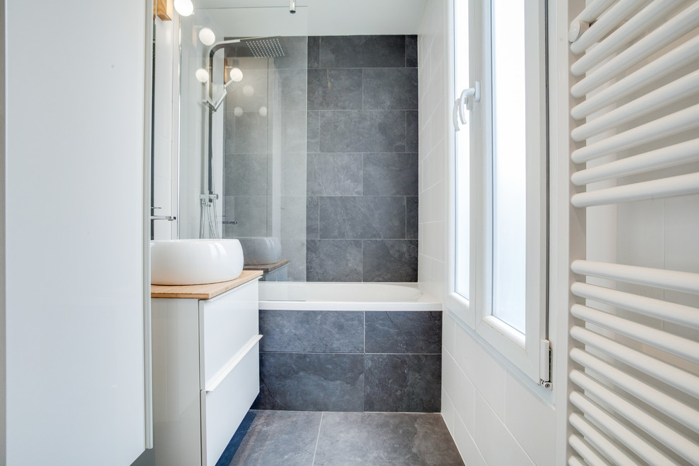 Cette image montre une petite salle de bain design avec des portes de placard blanches, une baignoire encastrée, WC suspendus, un carrelage noir et blanc, du carrelage en ardoise, un sol en ardoise, un lavabo posé, un plan de toilette en bois et un sol noir.