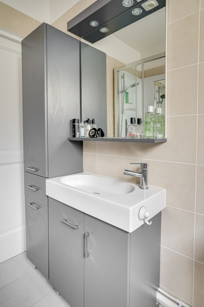 Bild på ett litet funkis beige beige badrum med dusch, med grå skåp, en hörndusch, en toalettstol med hel cisternkåpa, beige kakel, cementkakel, beige väggar, cementgolv, ett avlångt handfat, kaklad bänkskiva, grått golv och dusch med skjutdörr