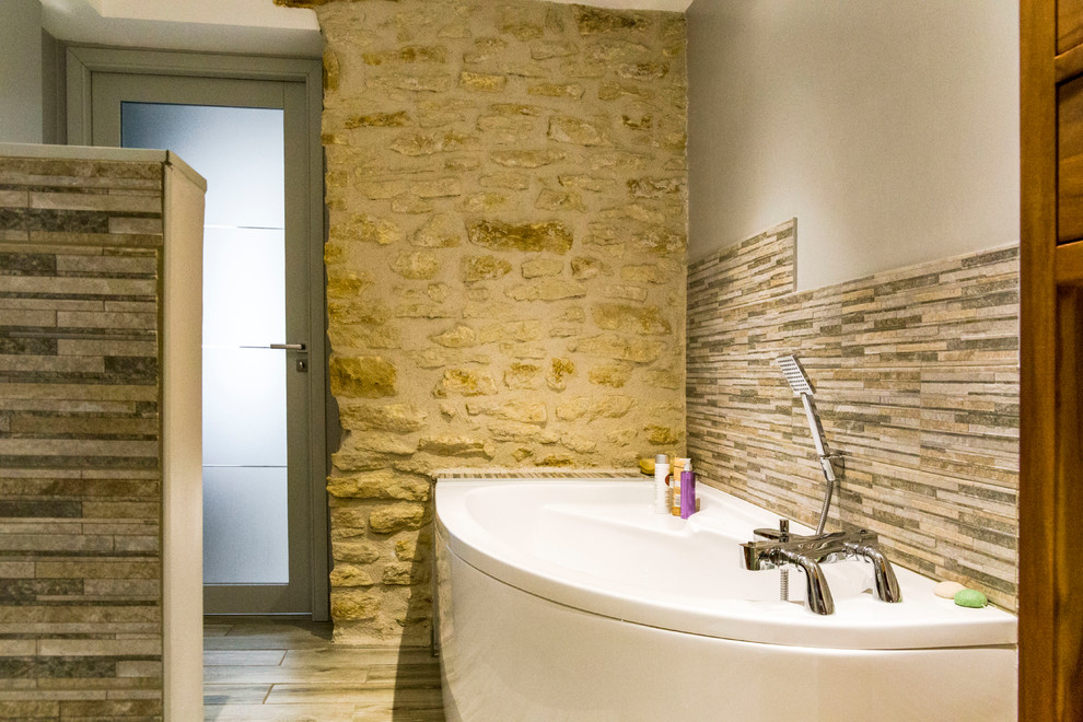 Modern inredning av ett mellanstort en-suite badrum, med ett hörnbadkar, en kantlös dusch, en toalettstol med separat cisternkåpa, flerfärgad kakel, stickkakel, grå väggar, klinkergolv i terrakotta, ett nedsänkt handfat, träbänkskiva, beiget golv och med dusch som är öppen