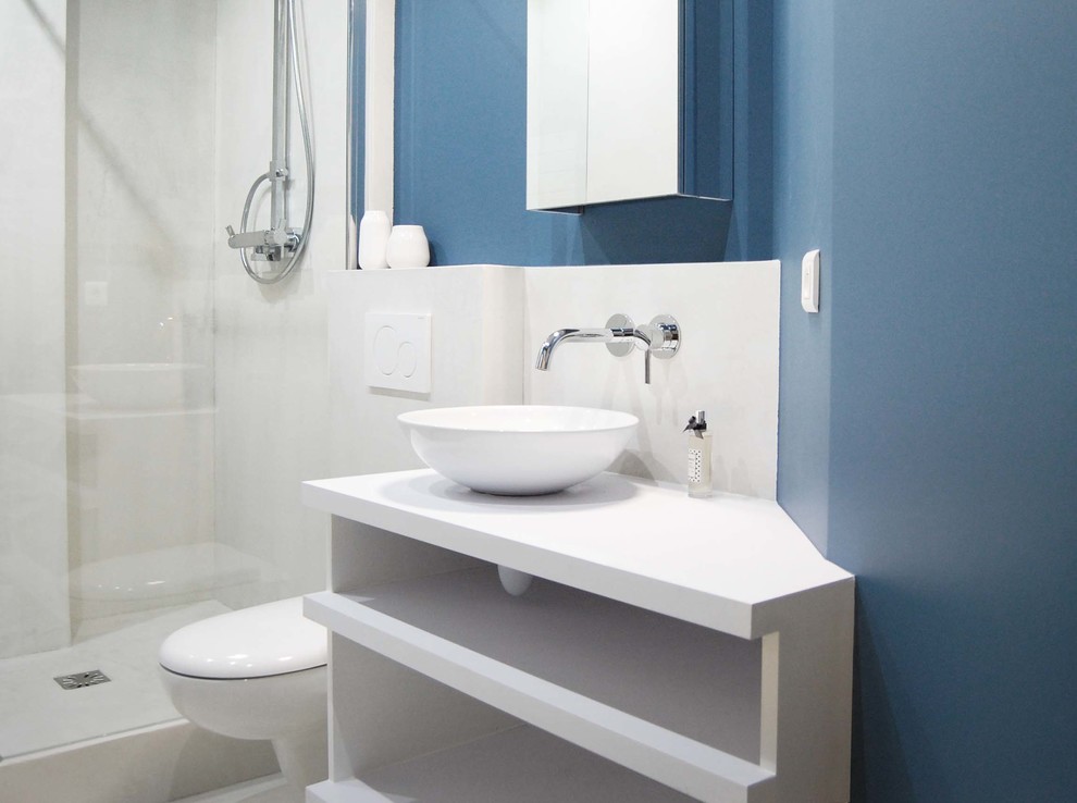 Foto på ett mellanstort funkis badrum med dusch, med en vägghängd toalettstol, blå väggar, betonggolv, ett fristående handfat, bänkskiva i betong, öppna hyllor, vita skåp, en hörndusch och vit kakel