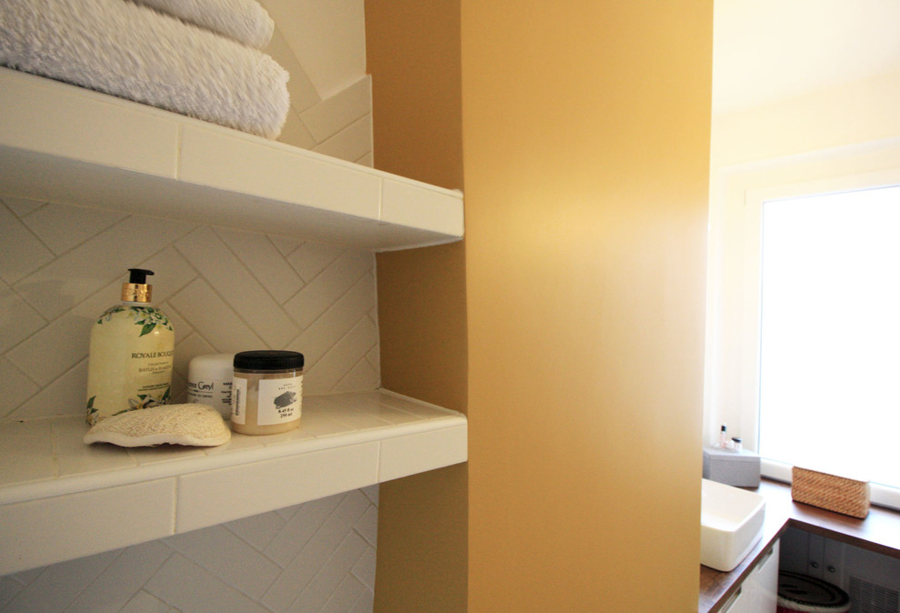 Bild på ett litet retro badrum, med luckor med profilerade fronter, vita skåp, ett undermonterat badkar, våtrum, vit kakel, stickkakel, gula väggar, cementgolv, ett nedsänkt handfat, träbänkskiva och gult golv