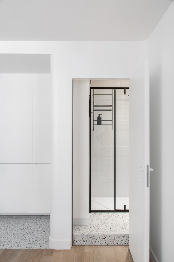 Modern inredning av ett litet beige beige badrum med dusch, med en kantlös dusch, en vägghängd toalettstol, vit kakel, keramikplattor, vita väggar, terrazzogolv, ett fristående handfat, träbänkskiva, flerfärgat golv och dusch med gångjärnsdörr