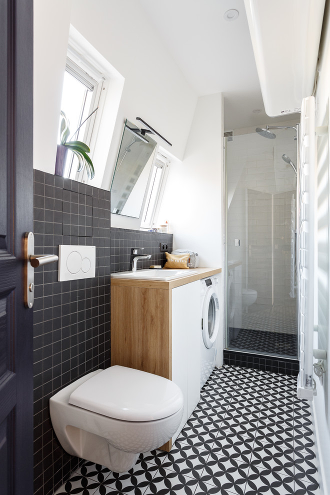 Inspiration for a small contemporary bathroom in Paris with flat-panel cabinets, white cabinets, a wall mounted toilet, black tiles, white tiles, white walls, a built-in sink, wooden worktops, multi-coloured floors, a hinged door, brown worktops, an alcove shower, ceramic tiles and cement flooring.