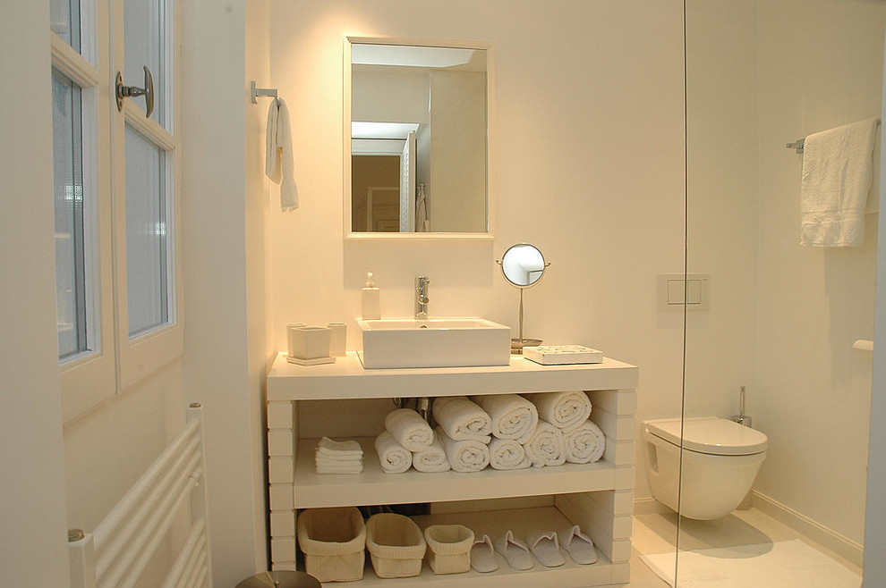 Foto de cuarto de baño rectangular actual de tamaño medio con aseo y ducha, armarios abiertos, sanitario de pared, paredes blancas, lavabo sobreencimera y puertas de armario blancas