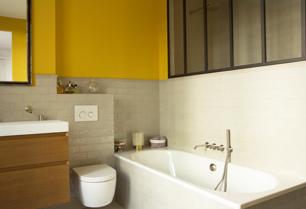 Пример оригинального дизайна: главная ванная комната среднего размера в стиле фьюжн с плоскими фасадами, светлыми деревянными фасадами, полновстраиваемой ванной, инсталляцией, белой плиткой, плиткой кабанчик, желтыми стенами, полом из цементной плитки, врезной раковиной и белым полом