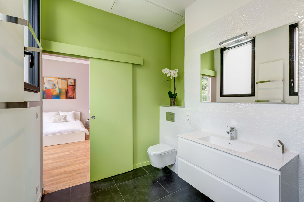 Immagine di una stanza da bagno padronale design di medie dimensioni con pareti verdi, WC sospeso, piastrelle bianche, lavabo integrato e pavimento con piastrelle in ceramica