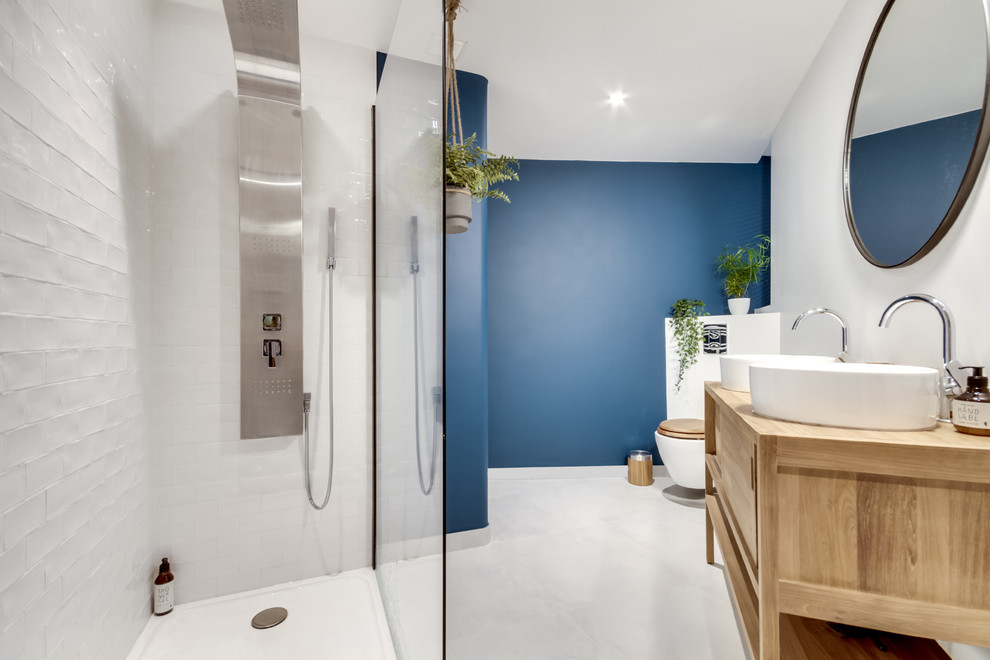 Photo of a medium sized contemporary shower room bathroom in Paris with a corner shower, a wall mounted toilet, white tiles, metro tiles, blue walls, wooden worktops, grey floors, light wood cabinets, a vessel sink, an open shower, beige worktops, concrete flooring and flat-panel cabinets.