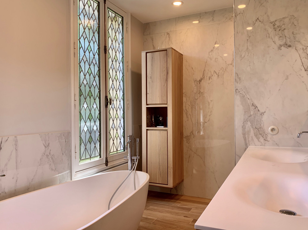 Idéer för ett mellanstort modernt vit en-suite badrum, med luckor med profilerade fronter, skåp i ljust trä, ett fristående badkar, en kantlös dusch, en toalettstol med separat cisternkåpa, vit kakel, marmorkakel, grå väggar, klinkergolv i keramik, ett konsol handfat, bänkskiva i akrylsten och med dusch som är öppen