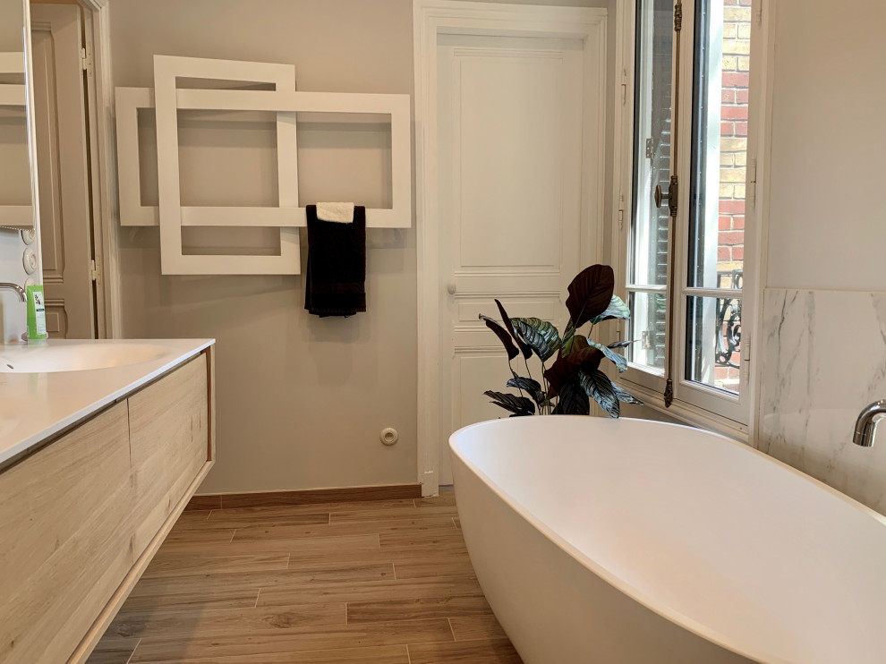 Bild på ett mellanstort funkis vit vitt en-suite badrum, med luckor med profilerade fronter, skåp i ljust trä, ett fristående badkar, en kantlös dusch, en toalettstol med separat cisternkåpa, vit kakel, marmorkakel, grå väggar, klinkergolv i keramik, ett konsol handfat, bänkskiva i akrylsten och med dusch som är öppen