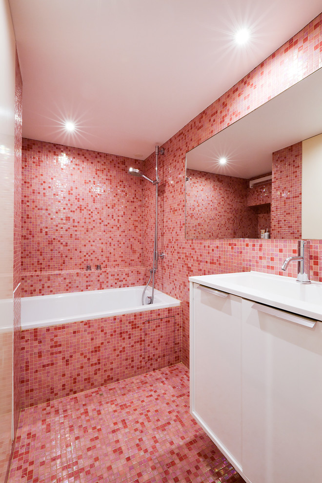 Cette image montre une petite salle de bain bohème pour enfant avec une baignoire encastrée, un carrelage rose, un mur rose, un plan vasque, un sol rose, aucune cabine, un plan de toilette blanc, un placard à porte plane, des portes de placard blanches, mosaïque, un sol en carrelage de terre cuite, un plan de toilette en surface solide et un espace douche bain.