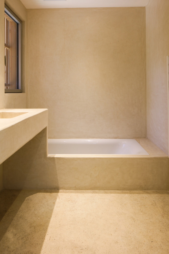 Aménagement d'une salle de bain principale exotique avec un placard sans porte, une baignoire encastrée, WC séparés, un mur beige, sol en béton ciré, un plan vasque, un plan de toilette en surface solide, un sol beige, un plan de toilette beige et meuble simple vasque.