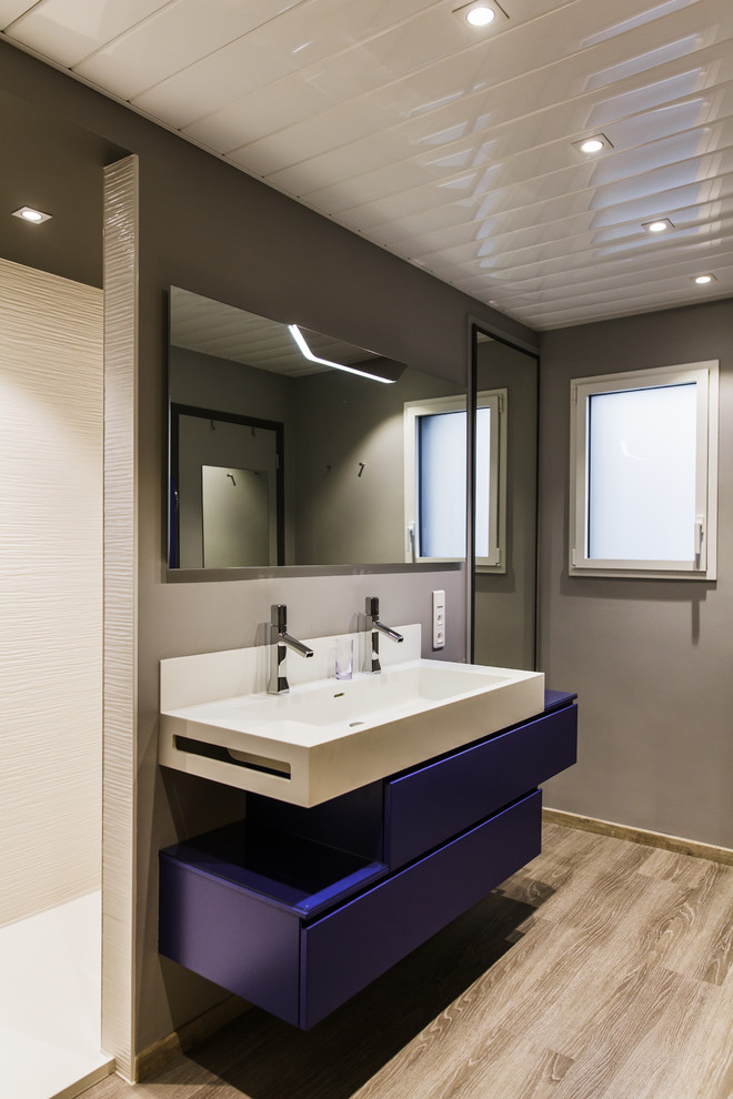 Exempel på ett mellanstort modernt en-suite badrum, med luckor med profilerade fronter, blå skåp, en kantlös dusch, en vägghängd toalettstol, vit kakel, keramikplattor, vita väggar, målat trägolv, ett konsol handfat, bänkskiva i akrylsten, grått golv och med dusch som är öppen
